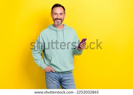 Photo of satisfied technology gadget user middle age man wear khaki hoodie hold phone browsing new dating app isolated on yellow color background