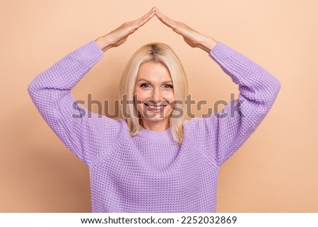 Photo of satisfied glad nice mature lady with blond hairdo wear knit sweater hold hands over head isolated on beige color background