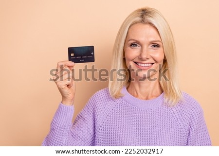 Photo of pleasant cheerful retired lady blond hairdo wear knit sweater hold plastic card online eshop isolated on beige color background