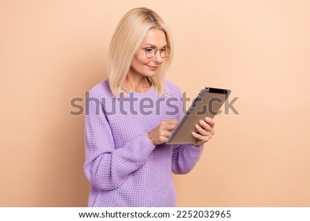 Photo of optimistic positive mature lady with blond hairdo wear knit sweater read post email in tablet isolated on beige color background