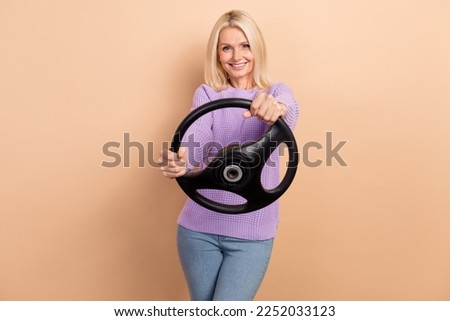Photo of satisfied cheerful lady with blond hairdo wear knit sweater hold steering wheel test drive isolated on beige color background