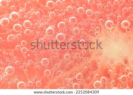 Slice of grapefruit in sparkling water. Grapefruit slice covered by bubbles in carbonated water. Grapefruit slice in water with bubbles. Color macro image of a grapefruit slice with detailed texture.