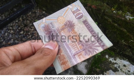 Saudi Arabia 10 riyals banknote in human hand on blurred background. Outdoor shoot.      Saudi Arabia 10 riyals banknote, The Saudi riyal is the currency of Saudi Arabia.