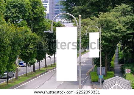 Tall vertical hanging blank advertising banners posters mockup; lush plants and tress in background; for OOH out of home lamp post media