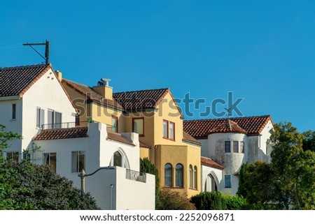 Row of modern houses in the historic districts of downtown san francisco california with front yard trees and blue sky. In late afternoon sun with visible power line pole and balconies.