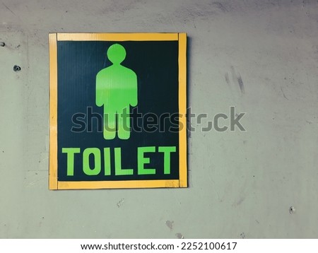 Toilet sign with yellow and green color on an old white wall.