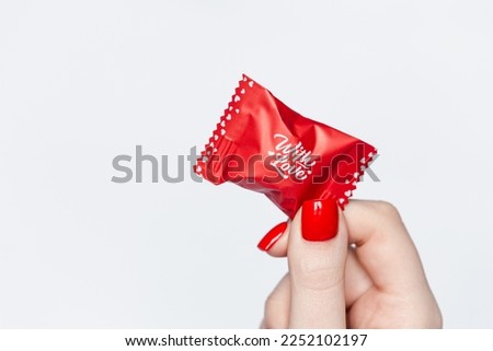 Woman's hand with red manicure, holding a candy with love lettering, isolated on white, Valentine's Day concept, copy space.