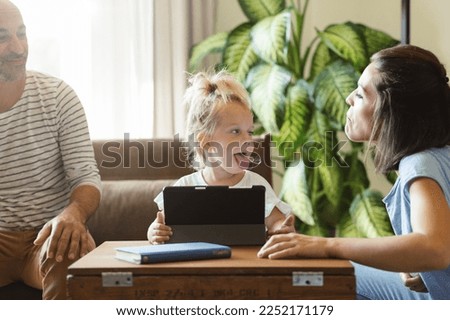 While watching cartoons on the tablet, the parents play with their daughter and make tongues at each other
