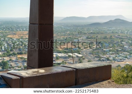 Rest stop or sitting area on a path in national park overlooking the downtown or suburban areas of Tuscon Arizona. In midday sun with rolling hills and hazy blue sky in shade with sun ontop of hill.