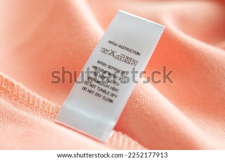White laundry care washing instructions clothes label on pink cotton shirt