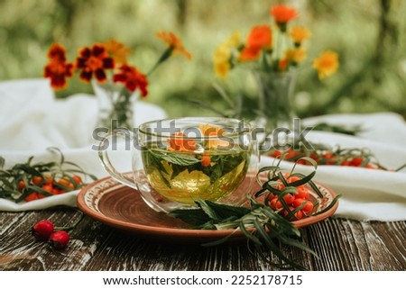herbal tea of mint, calendula and sea buckthorn berries in a glass transparent cup on a brown wooden table. Alternative medicine.
 Natural pharmacy. Bouquets of wild herbs