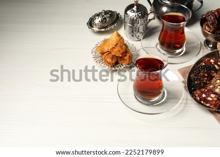 Glasses of tea, baklava dessert, Turkish delight and date fruits served in vintage tea set on white wooden table, space for text
