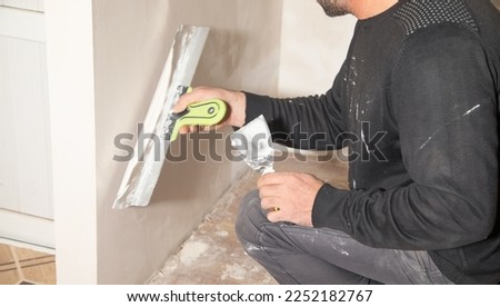Worker is applying putty on a wall. Renovating house  Royalty-Free Stock Photo #2252182767
