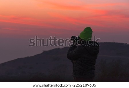 Silhouette of a woman photographer in a green hat with a camera while taking a photo at sunset