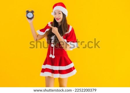Portrait beautiful young asian woman wear christmas clothes and hat show clock or alarm on yellow isolated background