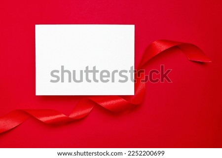 Card mockup, blank flyer with ribbon on red background, top view, flat lay. Blank invitation, holiday greeting card mockup with copy space