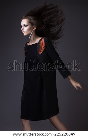 Stylish girl in a fashionable autumn clothes and bright make-up with the wind in her hair. Picture taken in the studio on a gray background.