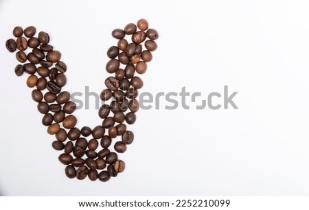 V is a capital letter of the English alphabet made up of natural roasted coffee beans that lie on a white background. Plenty of space to put text or pictures, top view and studio photography.