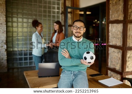 Portrait of young businessman with football ball in coworking space