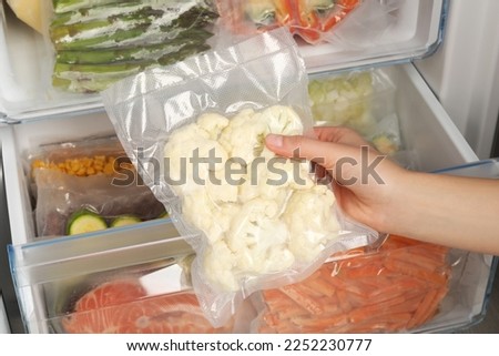 Woman putting vacuum bag with cauliflowers into fridge, closeup. Food storage Royalty-Free Stock Photo #2252230777