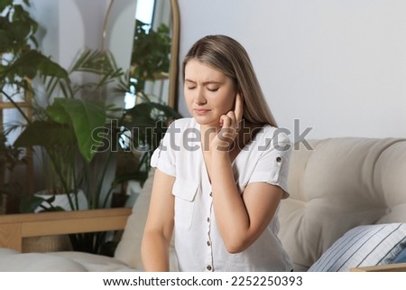 Young woman suffering from ear pain at home Royalty-Free Stock Photo #2252250393