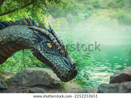 Fantasy art portrait real dragon head close-up sharp teeth beautiful eyes muzzle in dark gray-green scales, spikes. Creative big dinosaur toy of Jurassic period. Background summer nature green trees.