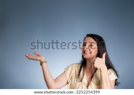 Portrait of young beautiful woman with her palm stretched out to the side. Isolated against light blue background.