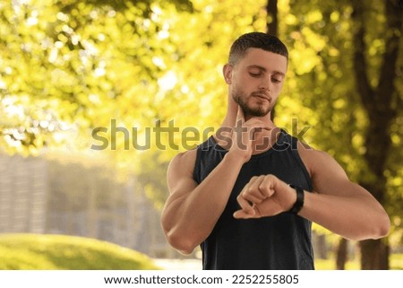 Attractive serious man checking pulse after training in park on sunny day. Space for text