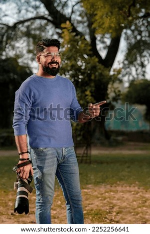 Young indian man holding camera in hand and giving expression at park