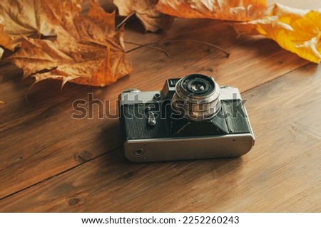 Autumn composition. Retro camera, autumn leaves, checkers on a wooden background. The view from top.