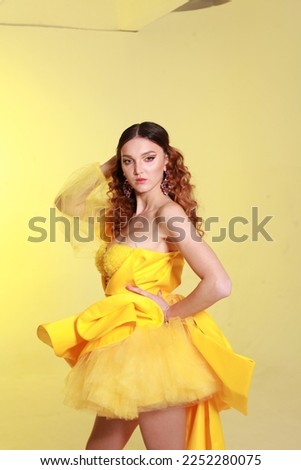 Summer fashion concept: runway woman skinny model with vitiligo  wearing monochrome yellow couture outfit with long skirt, posing in studio on yellow background. 
Photo catalog clothes style