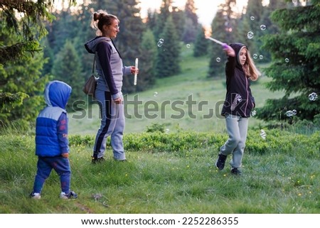 Mother plays with daughter and son in soap bubbles in a forest during an walk