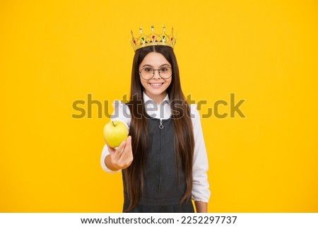 Princess child in queen crown hold apple isolated on yellow background. Teenage girl wear diadem. Happy girl face, positive and smiling emotions.