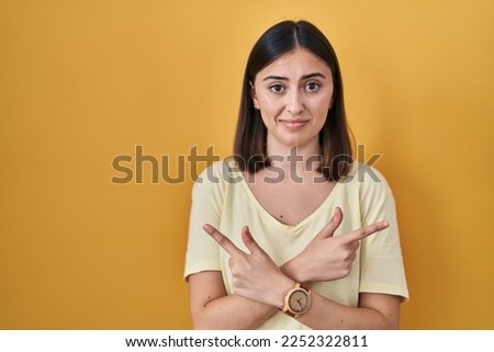 Hispanic girl wearing casual t shirt over yellow background pointing to both sides with fingers, different direction disagree 