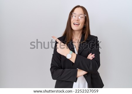 Beautiful brunette woman wearing business jacket and glasses with a big smile on face, pointing with hand finger to the side looking at the camera. 