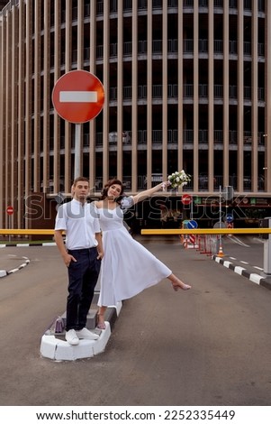 The bride and groom hung on a road stop sign near the entrance to a multi-storey parking lot. Slightly drunk newlyweds brawl in the city. Wedding in urban style. Selective focus