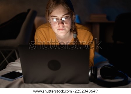 Young student girl lying with laptop on bed in student dormitory at late night. Copy space
