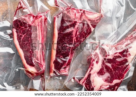 Dry aged steak in a vacuum. Meat products in plastic pack set, tomahawk, t bone and club steak cuts, on old dark rustic background, top view flat lay Royalty-Free Stock Photo #2252354009