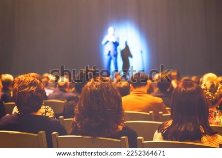 Man appears on stage in theater with a lot of people.