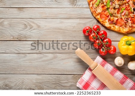 Pizza, tomatoes, mushrooms, bell pepper and rolling pin on wooden table background. Top view with copy space