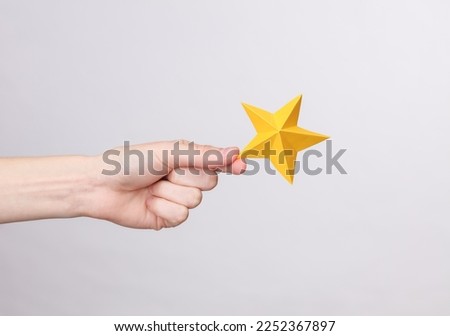 Woman's hand holds one paper star on a gray background. Service rating