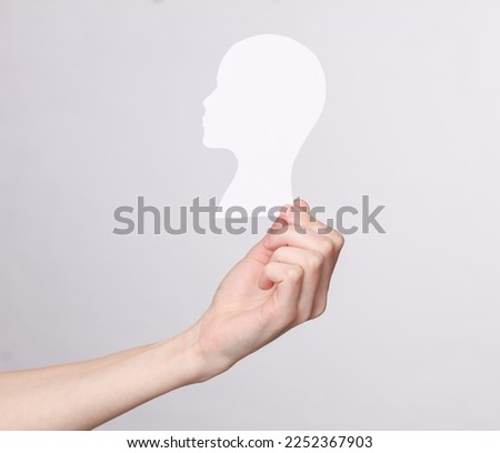 Woman's hand holding Paper cut white human head mockup on gray background