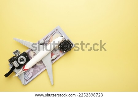 Flatlay picture of toy aeroplane, toy camera, luggage with fake money on copycapse yellow background. Expensive flight fare.
