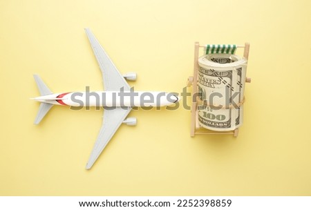 Flatlay picture of toy airplane, fake money and beach folding chair on yellow background