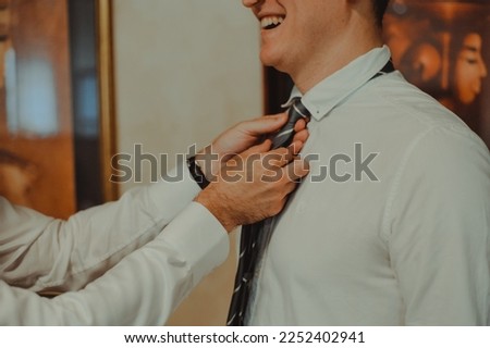 Stylish groomsmen helping happy groom getting ready in the morning for wedding ceremony. Luxury man in suit in room.  Wedding day. Royalty-Free Stock Photo #2252402941