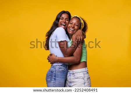 Two diversity pretty positive girls toothy smile hugging isolated on yellow color background. Young lesbian lovers couple embracing and looking camera. Friendship and homosexual relationship. Royalty-Free Stock Photo #2252408491