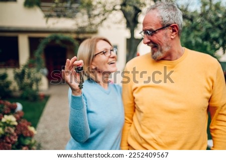 Senior couple holding up new house key while standing outside. Portrait of elderly mature caucasian husband and wife feeling happy about buying a new house. Focus on a keys in woman hands. Royalty-Free Stock Photo #2252409567