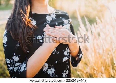 Hopeful woman putting hands on her chest in gratitude for God's blessings, in the field. Copy space Royalty-Free Stock Photo #2252437449