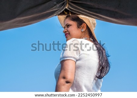 Attractive and Happy woman or lady with hat enjoys her tropical vacation on backwater of alleppey or Alappuzha from Houseboat. Selective focus on subject and background blur. Copy space