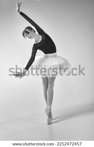 a ballerina in a black bodysuit and tutu poses in motion showing ballet elements while standing on pointe shoes